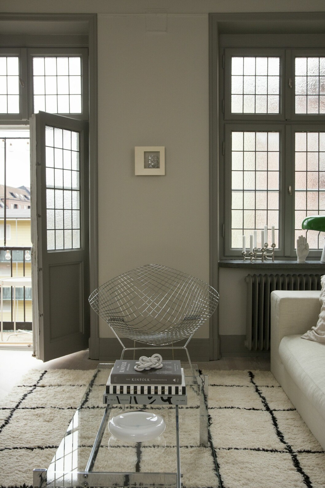 Nellie och Alexander valde rummet med balkong och blyinfattade fönster till sitt vardagsrum; lagom stort och med milt ljusinsläpp. Soffa, Hemdesigners. Glasbord, second hand. Harry Bertonias Diamond chair, hittades på Marketplace. Marockansk matta. Liten skulptur från Tufva design. Glasskål, second hand. Våningen med det lilla extra – hemma hos inredaren Nellie Fasth