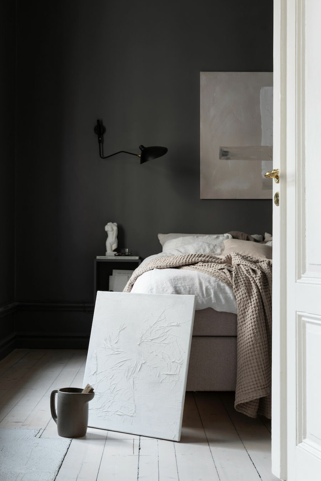 Tavla av Lovisa Häger för Wall of Art lutad mot säng i mörkt sovrum.